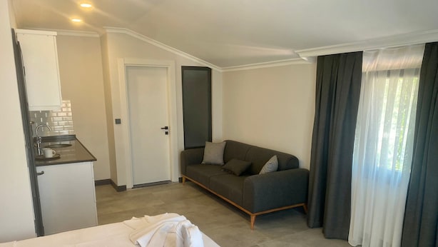 A hotel room with a bed, a sofa, a kitchenette, and a window with curtains. - Sönmez Güler Pansiyon Ölüdeniz (Muğla)