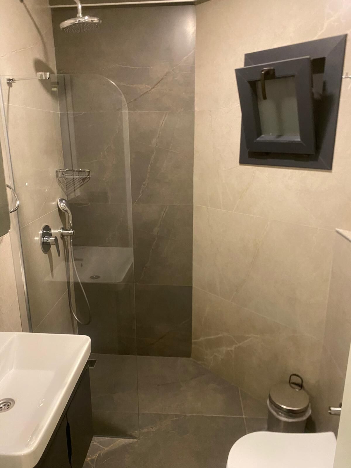 Een badkamer met douche, toilet en wastafel.