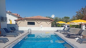 A swimming pool with lounge chairs and umbrellas, surrounded by buildings. - Sönmez Güler Pansiyon Ölüdeniz (Muğla)