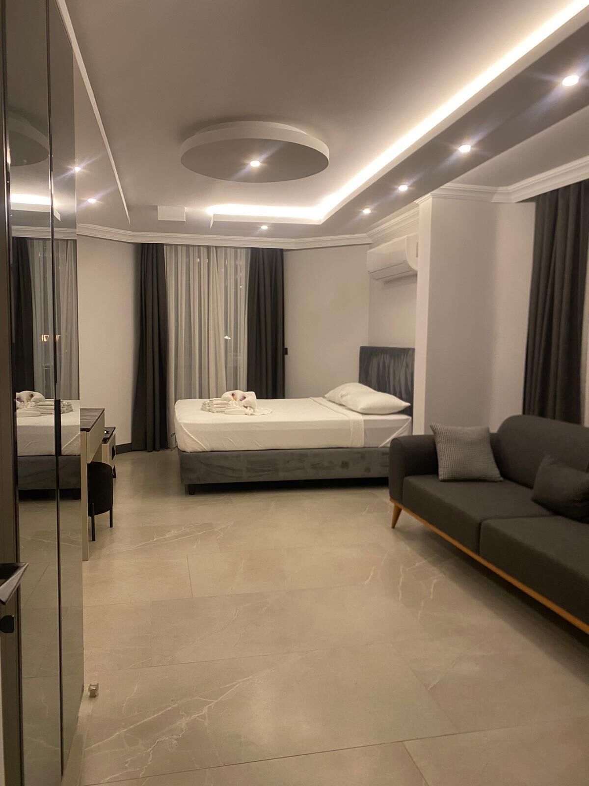 A modern bedroom with a bed, a sofa, a desk, and a mirror.