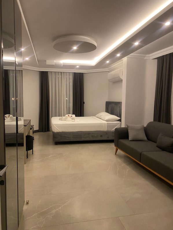 A modern bedroom with a bed, a sofa, a desk, and a mirror. - Sönmez Güler Pansiyon Ölüdeniz (Muğla)