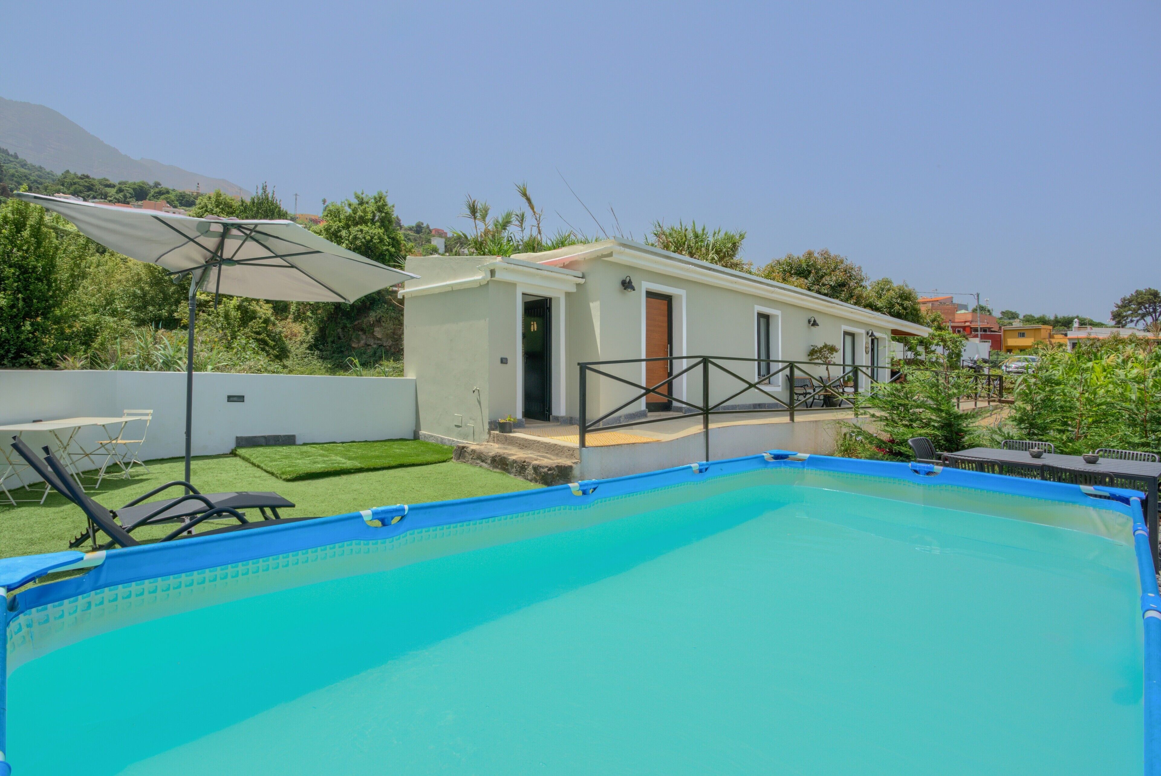 A swimming pool with a small building adjacent to it, a covered seating area, and a view of a mountainous landscape.