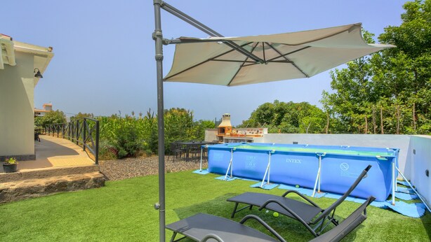 Een achtertuin met kunstgras, een zwembad, ligstoelen en een pergola met een parasol.