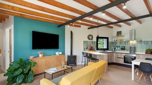 Een moderne keuken met een centraal eiland, een zithoek met gele sofa’s, en een flatscreen televisie aan de muur.