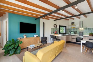 Eine moderne Küche mit einer zentralen Kochinsel, einem Essbereich mit gelben Sofas und einem an der Wand montierten Flachbildfernseher.
