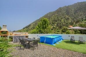 Eine Terrasse mit Tisch und Stühlen, ein Grill, ein blauer Pool und Blick auf einen bewaldeten Hügel.