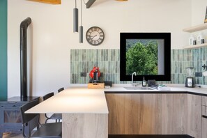 A modern kitchen with a central island, a built-in stove, and a large window with a view of greenery. -  'El Llano' with Sea View, Private Pool and Wi-Fi (La Orotava)