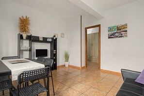A dining area with a table, chairs, a TV, and a potted plant. - Casa Levante Conil – Cozy Apartment in the Heart of Conil de la Frontera (Conil de la Frontera)