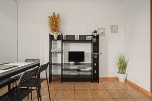 Ein Zimmer mit einem schwarzen Fernsehschrank, einem Esstisch mit Stühlen und einer Topfpflanze.