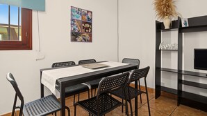 Zona pranzo con tavolo, sedie, un quadro appeso al muro e una libreria nera con un televisore.