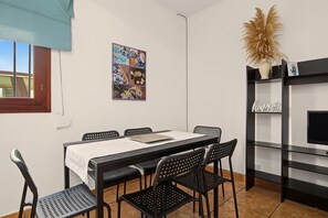 Ein Essbereich mit Tisch, Stühlen, einem Wandbild und einer schwarzen Regaleinheit mit Fernseher.