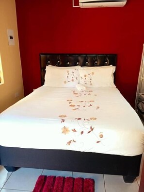 Una cama con una colcha estampada, una alfombra roja y un aire acondicionado de pared.