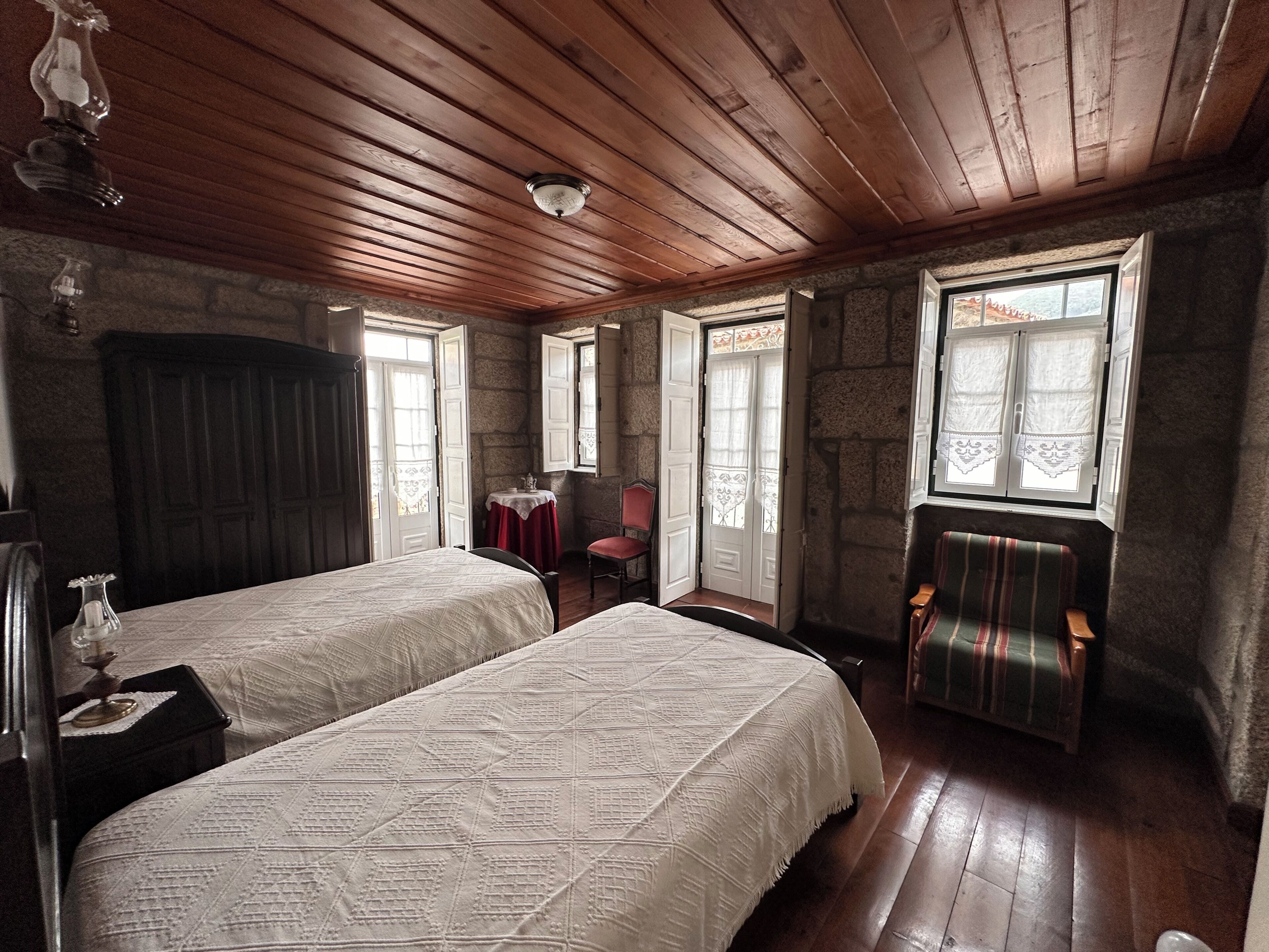 A room with two beds, a table with a vase, and a chair.