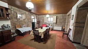 A dining area with a table set for four, surrounded by chairs, in a room with stone walls and wooden ceiling. - Casa João Fidalgo (Arcos de Valdevez)
