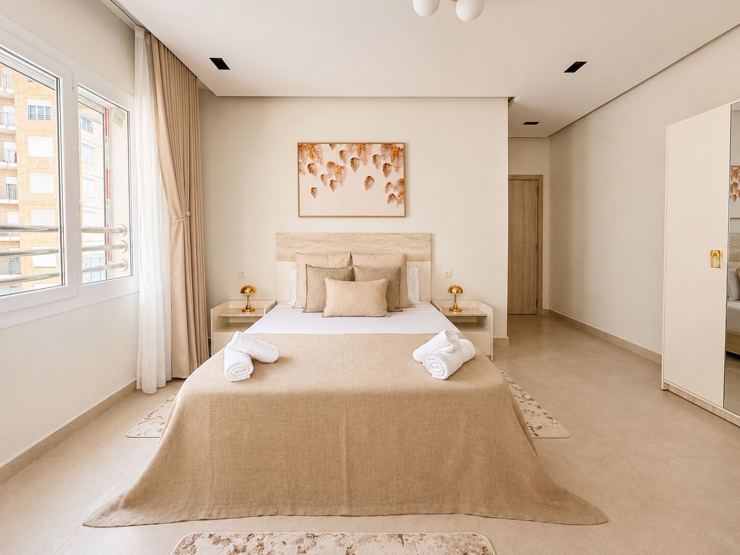 A modern bedroom with a large bed, two bedside tables, a headboard, and a window with curtains.