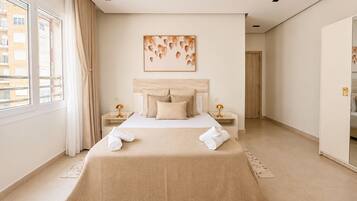 A modern bedroom with a large bed, two bedside tables, a headboard, and a window with curtains.