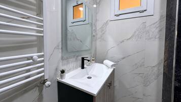 A bathroom with a white sink, a mirror, a towel, and a shower area.