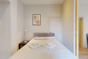 Habitación de hotel con una cama, una lámpara de noche, una obra de arte enmarcada en la pared y una puerta que da a otra habitación.