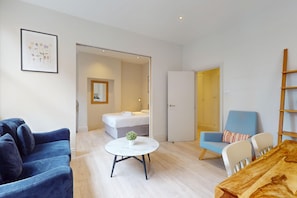 Una sala de estar moderna con un sofá azul, una mesa redonda de centro con una planta, un sillón azul y una mesa de comedor de madera.