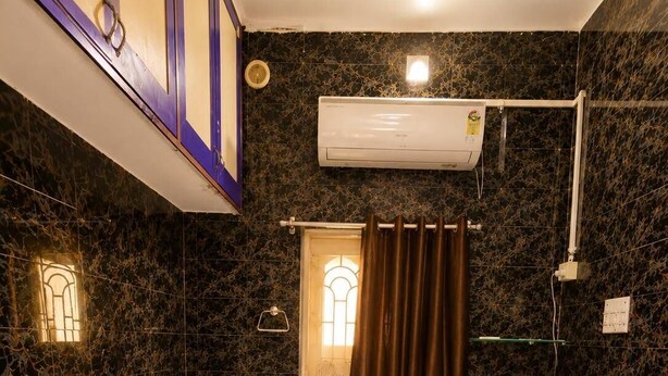 Habitación de hotel con dos camas individuales, una ventana con cortinas, un equipo de aire acondicionado y una lámpara de pared.