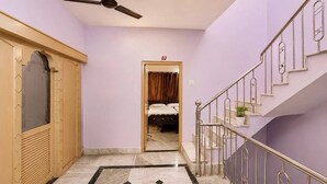 Un pasillo con ventilador de techo, una escalera con barandillas de metal y una cama visible a través de una puerta abierta.