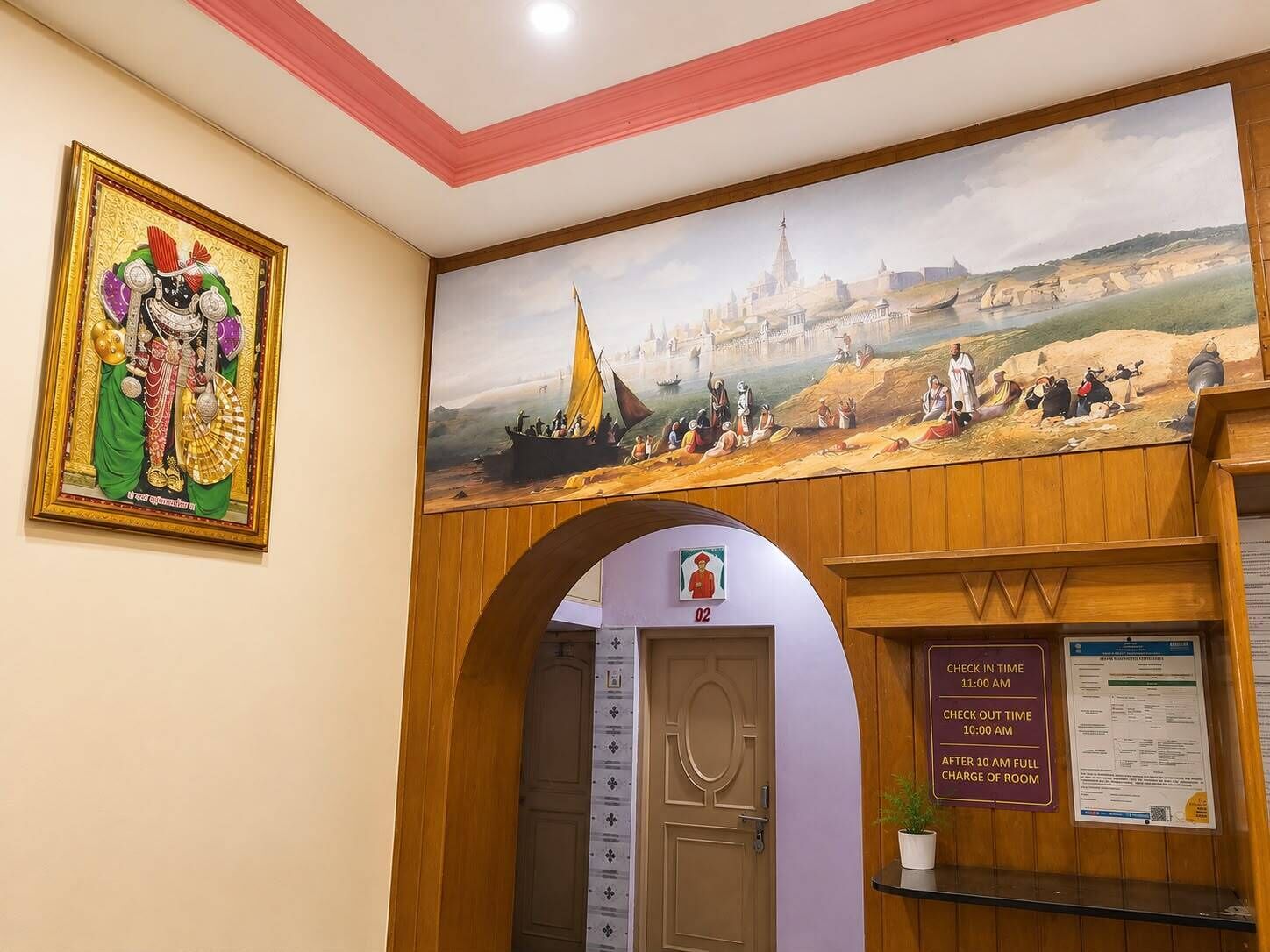 Uma área de recepção de hotel com um mural, um aviso de check-in/check-out e uma porta que dá para os quartos.