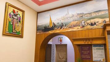 Uma área de recepção de hotel com um mural, um aviso de check-in/check-out e uma porta que dá para os quartos.