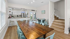 A modern kitchen with white cabinets, a wooden dining table, and a staircase leading to an upper level. - Dog Friendly Beach House 200ft From the Beach (Gulf Shores)