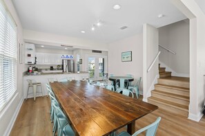 A modern kitchen with white cabinets, a wooden dining table, and a staircase leading to an upper level. - Dog Friendly Beach House 200ft From the Beach (Gulf Shores)