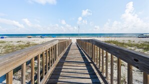A wooden boardwalk leading to a beach with clear skies and a flag. - Dog Friendly Beach House 200ft From the Beach (Gulf Shores)