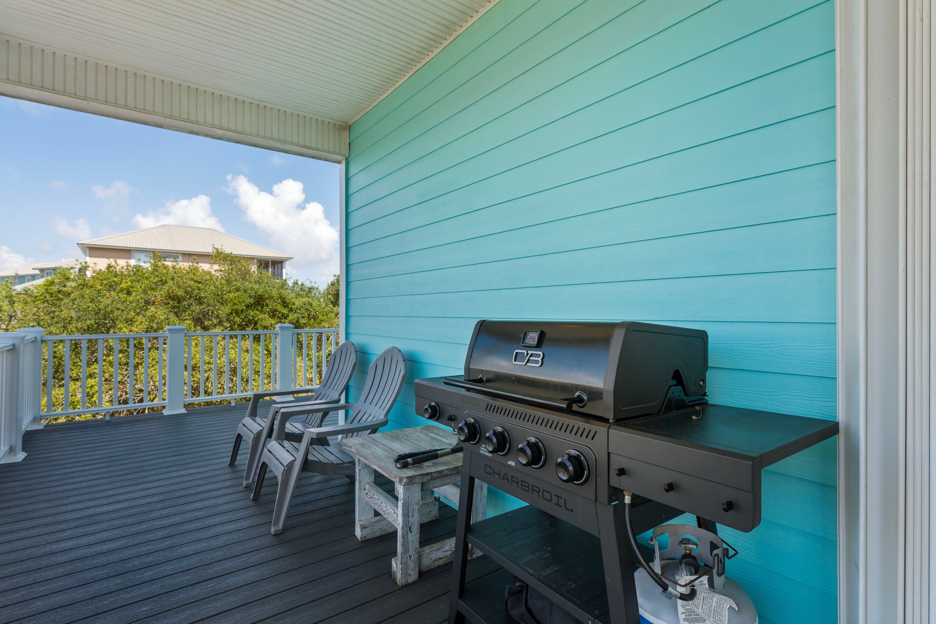 A covered outdoor area with a charcoal grill, two Adirondack chairs, and a view of a building in the background.