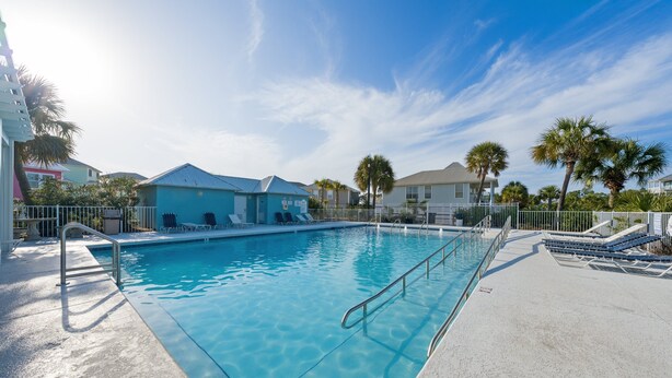 A clear swimming pool with a metal ladder, surrounded by a white fence, and palm trees in the background. - Dog Friendly Beach House 200ft From the Beach (Gulf Shores)