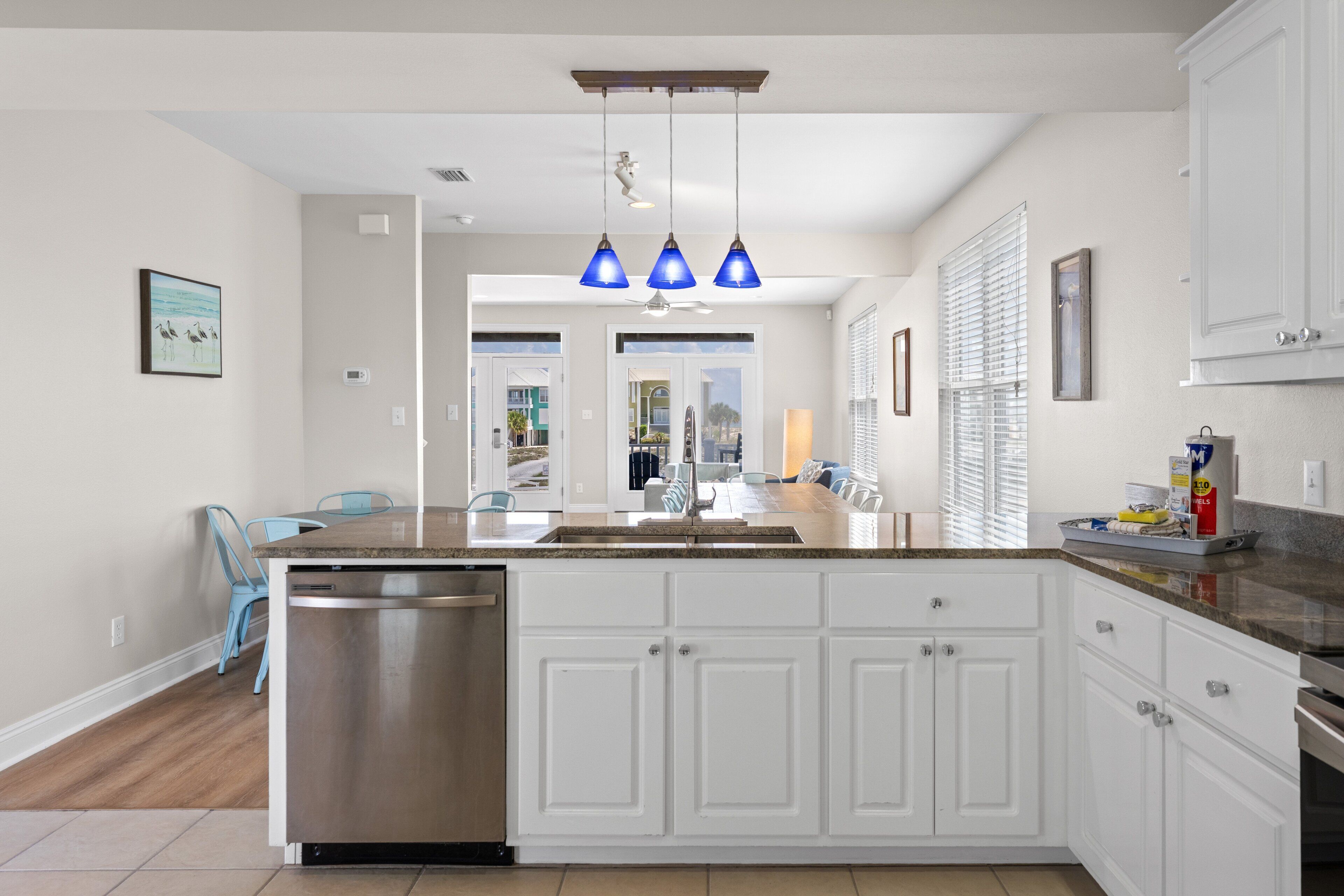 A modern kitchen with white cabinetry, a stainless steel dishwasher, and blue pendant lights.