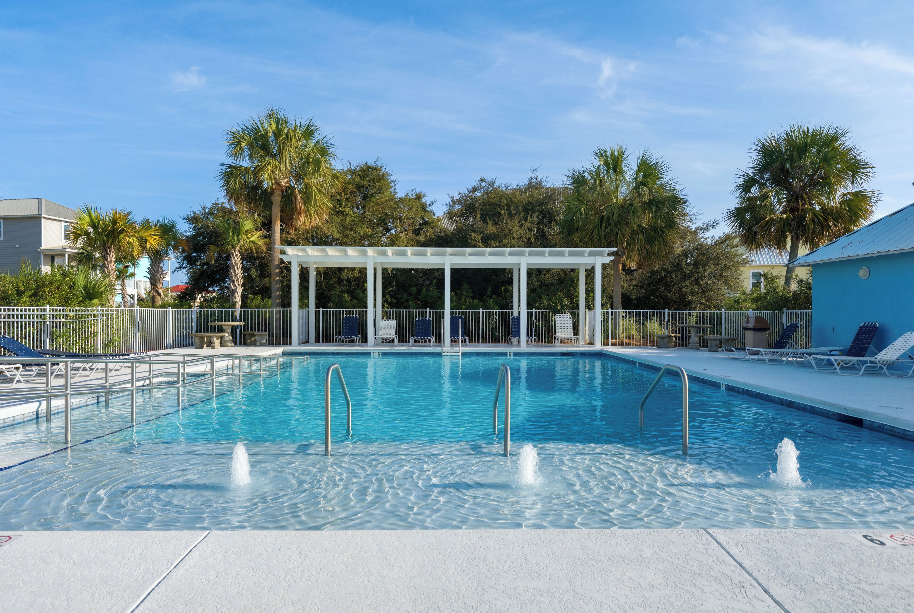 Une piscine dotée d’un espace détente couvert, entourée de palmiers et de chaises longues.