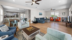 A spacious living area with a dining table, sofas, a coffee table with a chess set, and a kitchen in the background. - Dog Friendly Beach House 200ft From the Beach (Gulf Shores)