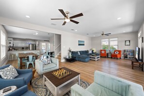 A spacious living area with a dining table, sofas, a coffee table with a chess set, and a kitchen in the background. - Dog Friendly Beach House 200ft From the Beach (Gulf Shores)