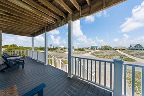 A covered outdoor area with a wooden deck, white railings, and a view of a coastal area with buildings. - Dog Friendly Beach House 200ft From the Beach (Gulf Shores)