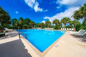 Ein rechteckiger Swimmingpool mit gefliestem Rand, umgeben von Liegestühlen und Palmen.