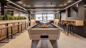 A billiards table with a pool cue and balls, surrounded by chairs and a bar area with stools. - Student Only Clarence Dock (Leeds)