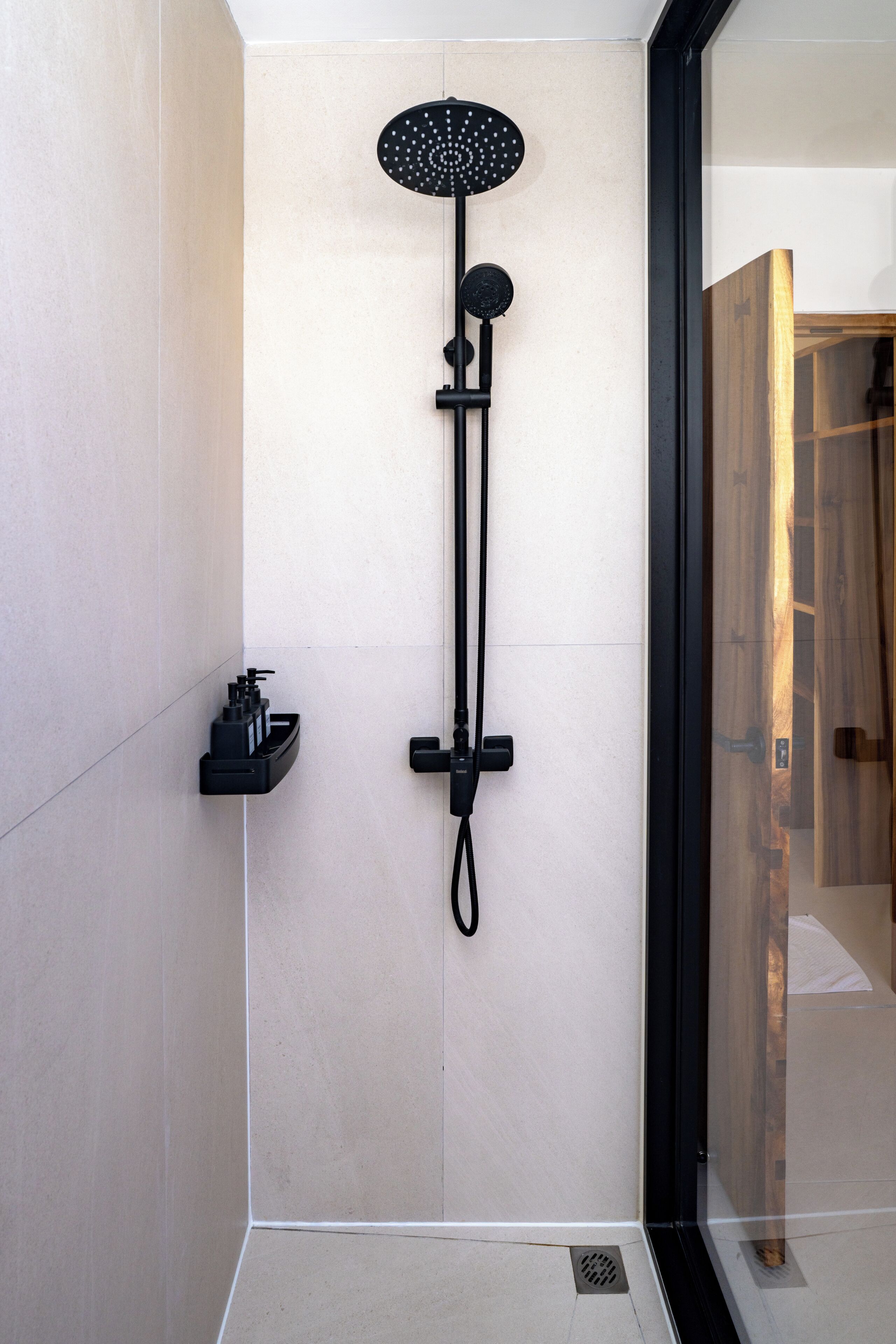 Ein modernes Badezimmer mit einer an der Wand montierten Duschkabine, einer kleinen Ablage für Toilettenartikel und einem Holztürrahmen.