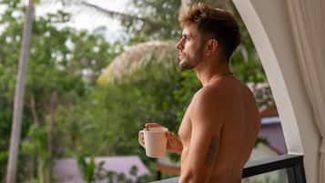 Un hombre de pie junto a una ventana con vista a palmeras y un paisaje tropical.