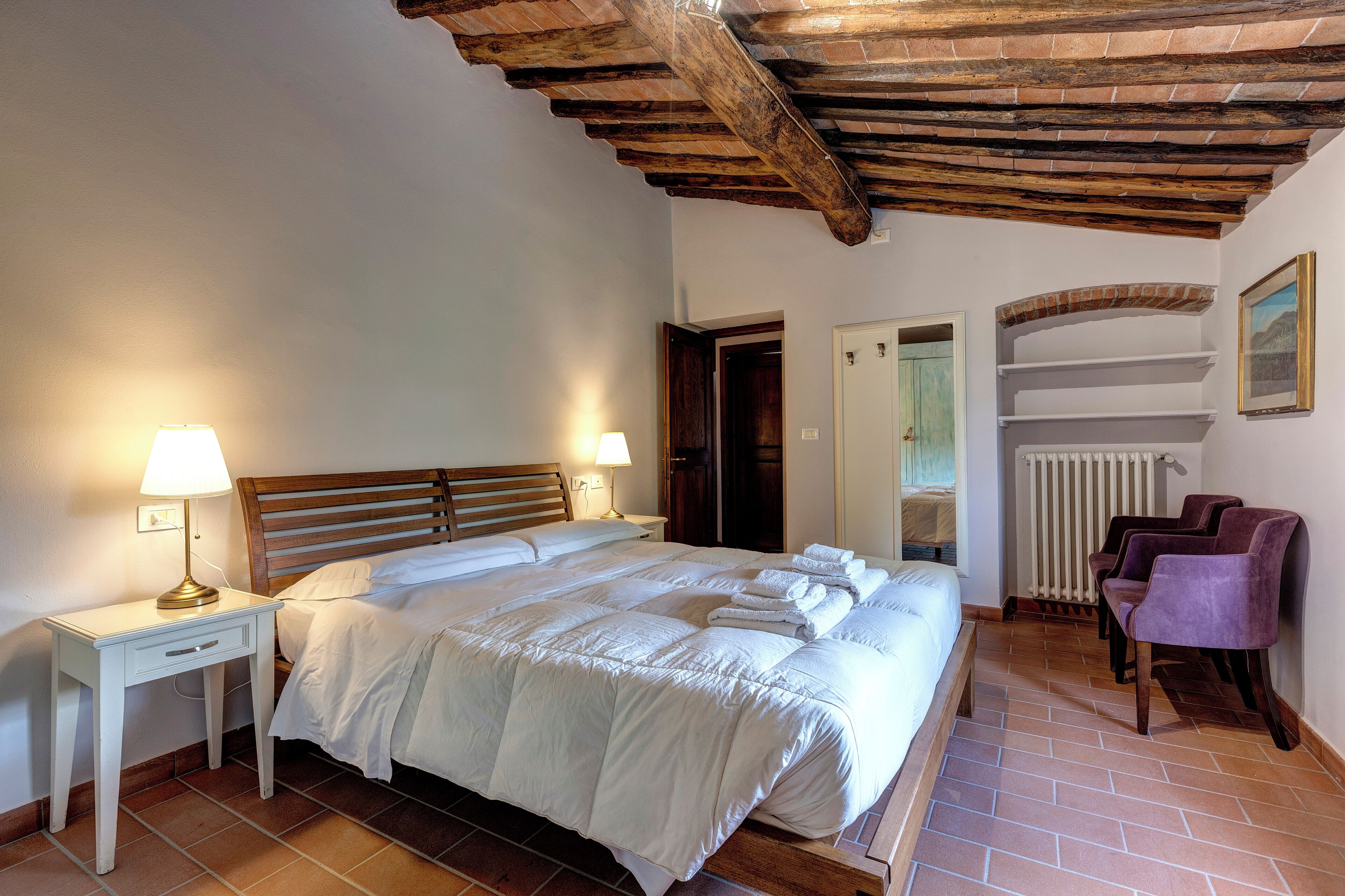 Une chambre à coucher avec un lit en bois, deux tables de chevet avec des lampes, un radiateur et une chaise.