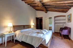 A bedroom with a wooden bed, two bedside tables with lamps, a radiator, and a chair. - Le Mortinete Farmstay: Olive Oil Mill (Toscana)