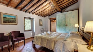 A bedroom with a large bed, a chair, a window, and a door leading to another room.