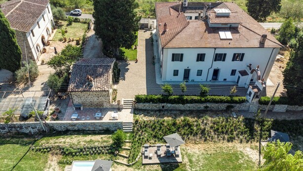 Un grande edificio con tetto in tegole, un muro in pietra e una zona verde con mobili da esterno.