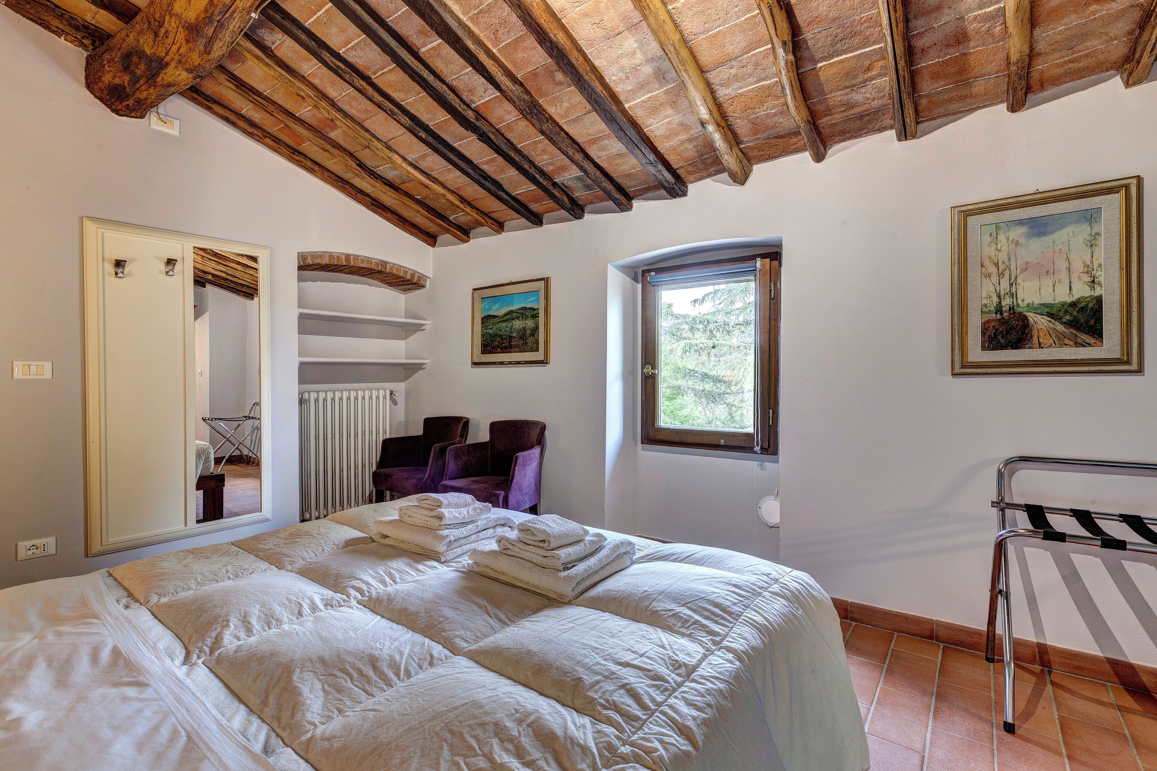 A bedroom with a large bed, a radiator, a window, and a door.