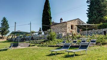 A stone building with a garden area featuring sun loungers and a stone wall.