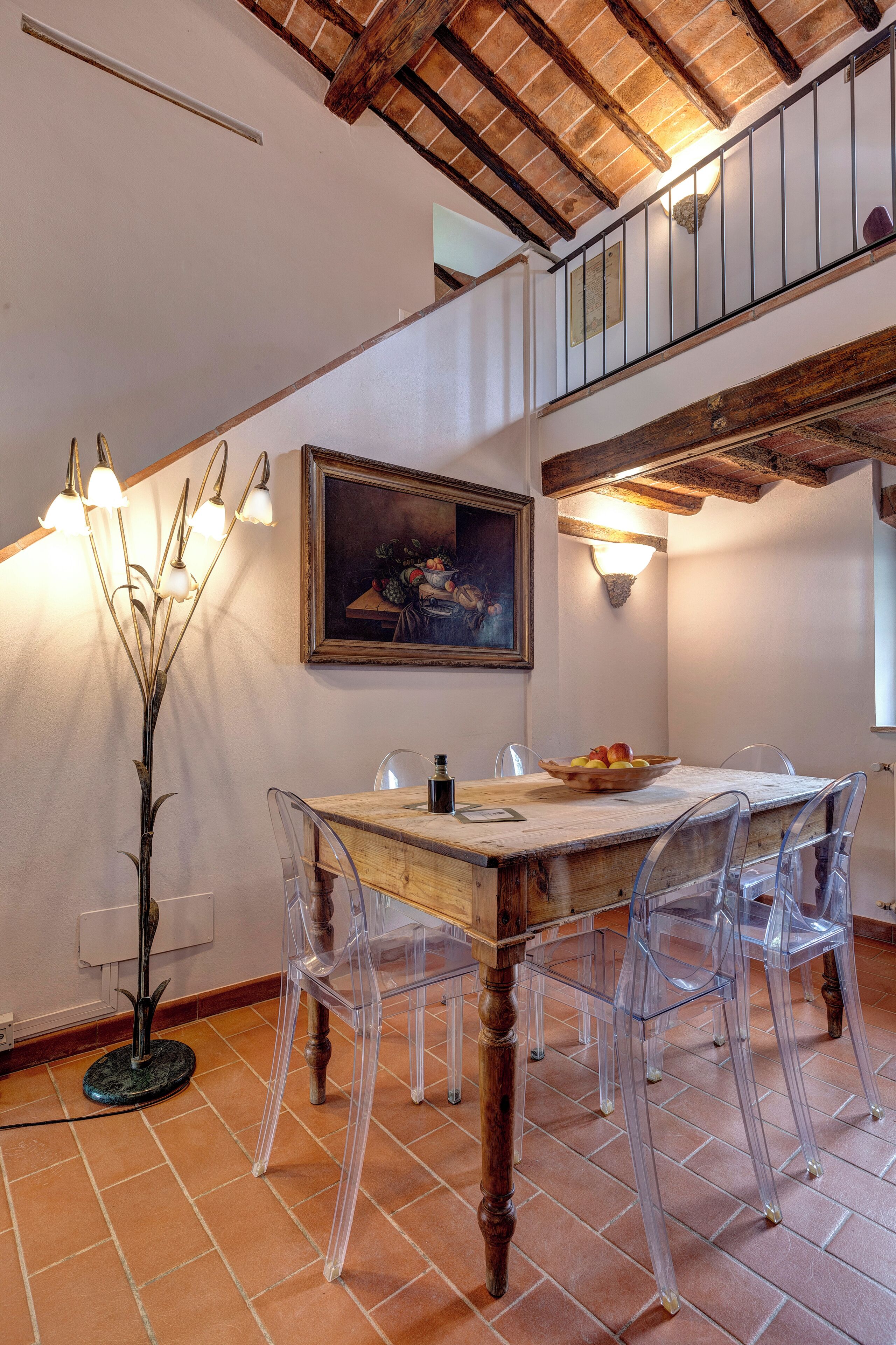 Un coin repas avec une table en bois, des chaises transparentes, un tableau au mur et une lampe sur pied.