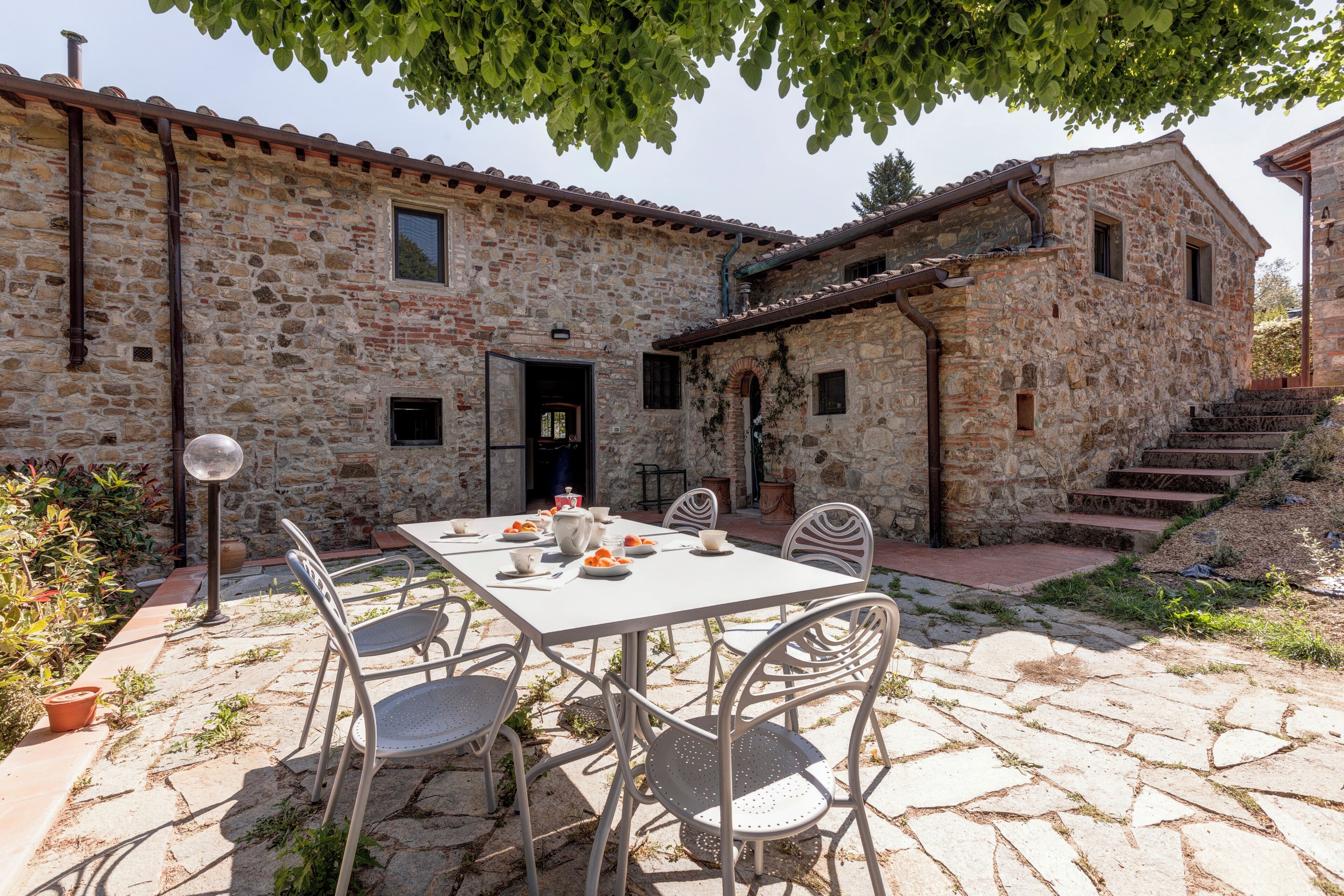 Un bâtiment en pierre doté d’une table et de chaises sur une terrasse, d’une porte et d’un escalier menant à un étage supérieur.