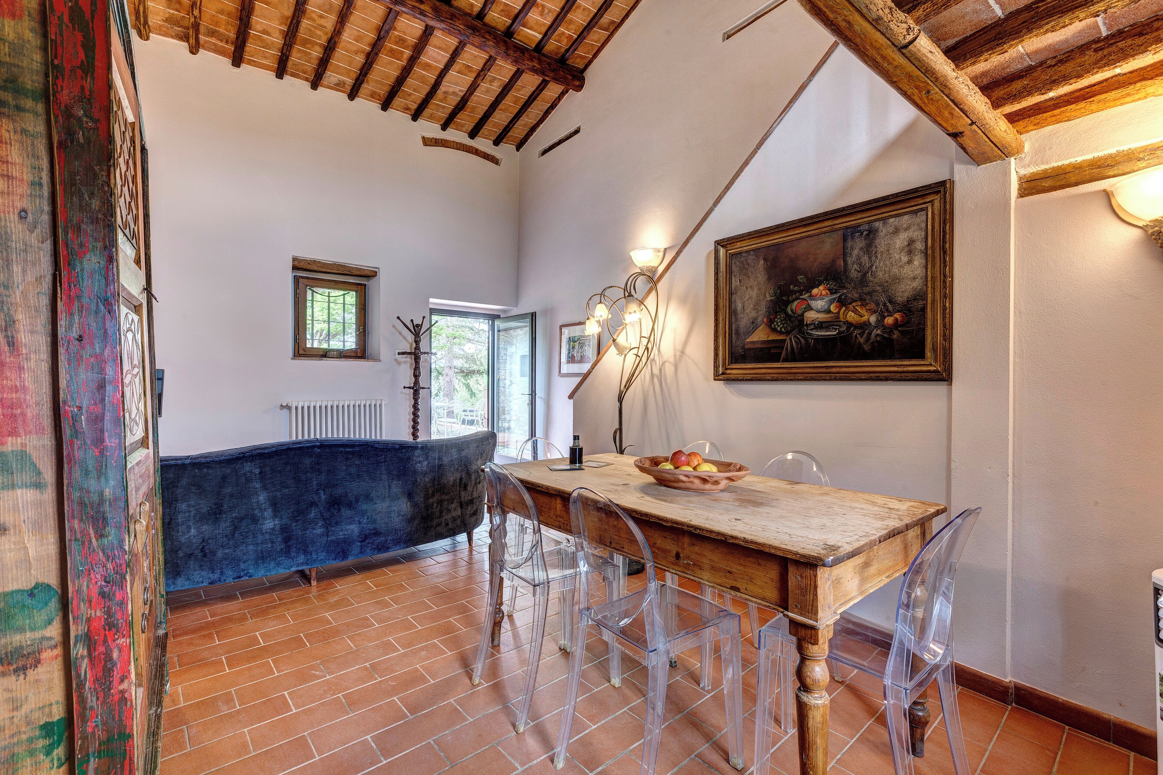 Un comedor con una mesa de madera, sillas transparentes, un cuadro en la pared y un techo rústico.